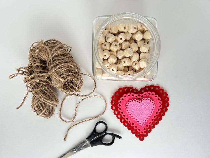 A top-down view of the materials needed for the craft including wooden beads, string, scissors, and felt hearts.