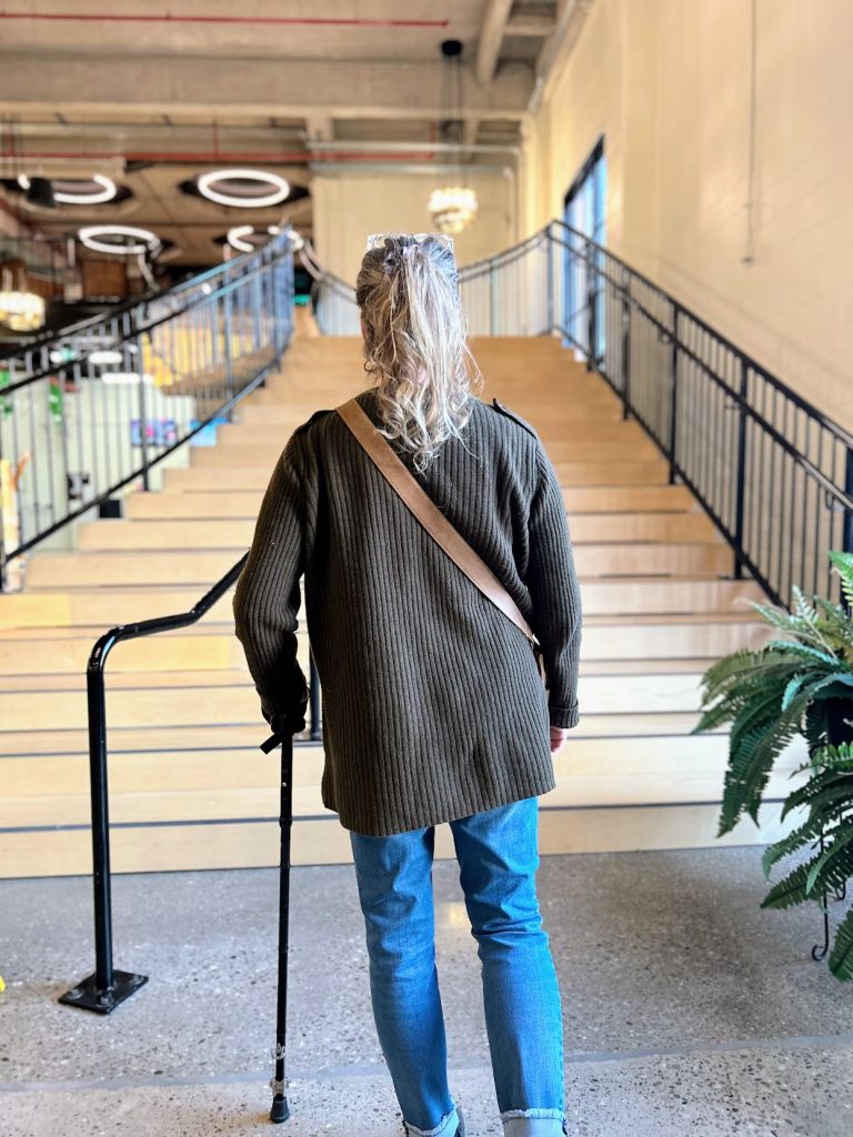 a woman with a cane stands at the base of a tall flight of stairs. 