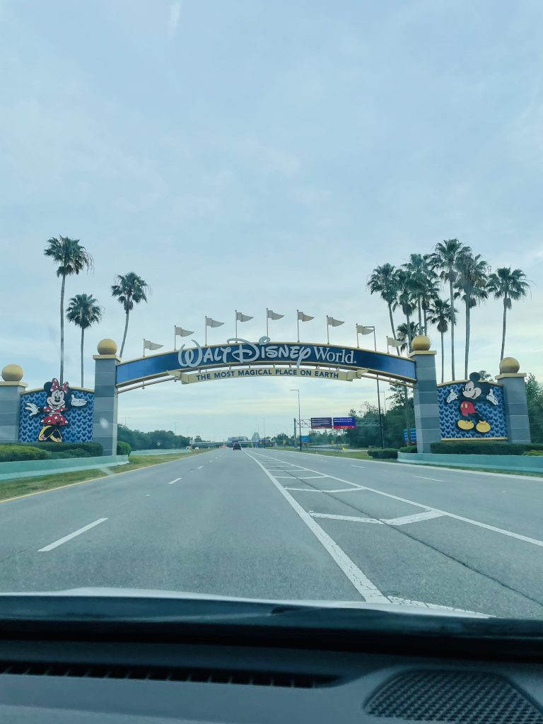 View from inside a car looking down a road to Walt Disney World entrance sign